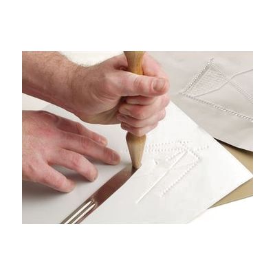 Two hands creating a tactile graphic of shapes and lines using the included hammer and tong tool on white paper.
