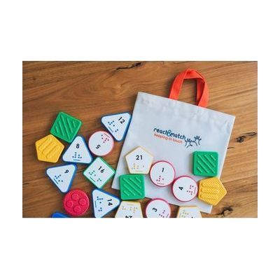 Reach & Match Number Tiles bag filled with multicolored Nemeth Number Tiles that are spilling out across a wooden surface.