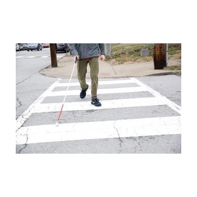 Photo of the legs and feet of a person with a white cane crossing at a cross walk.