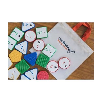 A variety of Reach and Match Alphabet Tiles laying on their canvas carrying case on a wooden floor.