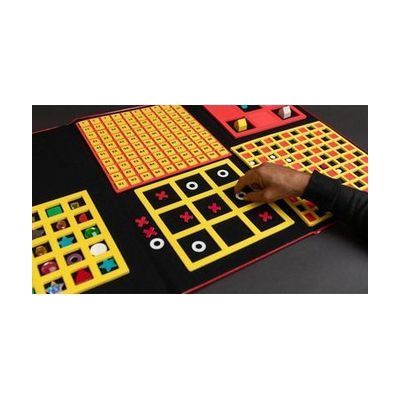 A hand placing a white circle in a yellow three-by-three grid in a game of tic tac toe. The grid is attached to a felt board that contains a variety of other grids used for different activities.
