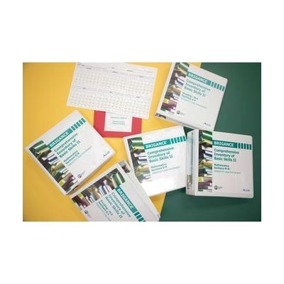 Five large print Brigance assessment binders, red mathematics foldout pages, and a calendar showing January through June rest on top of a yellow and green surface.