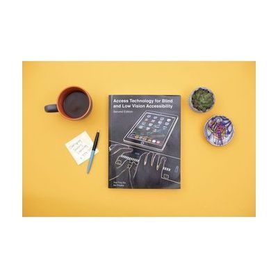 Image of book on table surrounded by coffee cup and plant.