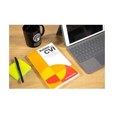 Babies with CVI book sits atop a desk, next to a laptop, APH mug, and pad of paper and pen