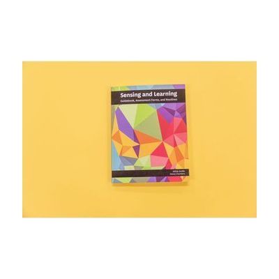 Sensing and Learning Guidebook, Assessment Forms, and Routines resting on a yellow background. The cover of the book showcases variations of pomegranate, teal, gold, and green.